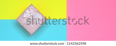Small pink gift box lie on texture background of fashion pastel blue, yellow and pink colors paper in minimal concept