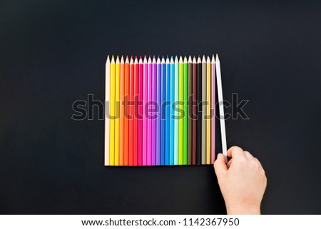 Kid hand choise colored pencil on black background Spectrum set background Close up Top view Copy space