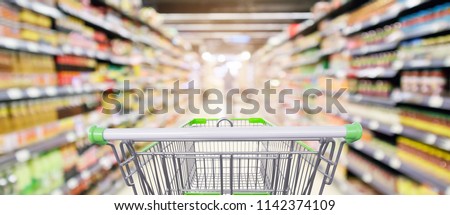 supermarket shelves aisle with empty shopping cart defocused interior blur bokeh light background Royalty-Free Stock Photo #1142374109