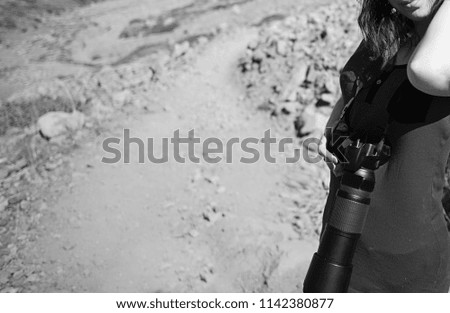 Girl photographer with a professional camera and a large lens on the background of a desert road in the mountains. Black and white photo.
