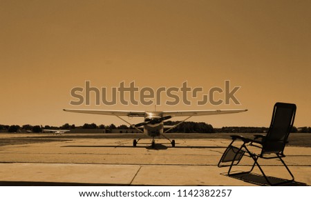 Two Planes. One in the Center of the Photo on the Background Airfield and the Second Aircraft. Armchair Beside Aircraft. Picture in the Sepia Style. Relaxation at the Airport. The Sun is at its Zenith
