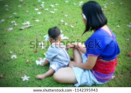 Blurring the mother and child sitting and relaxing on the lawn in a park in Thailand. 
