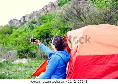 The girl is taking pictures near the tent. A woman is resting in nature. Camping in the forest. The brunette takes pictures of nature on the phone.