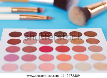 An eye level view of an eye shadow palette with brushes with a selective focus. The image composed over a bright blue background for sense of colorfulness.