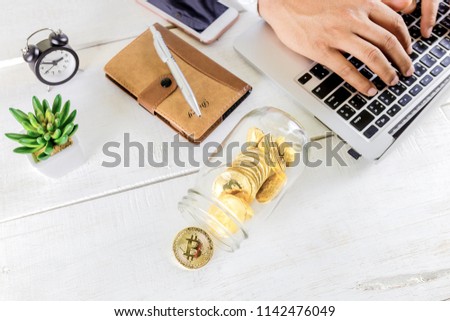 Bitcoin coin golden coin in the glass jar on wooden table ,Man using tablet for trading cryptocurrency or bitcion.Set of cryptocurrencies with a golden bitcoin 