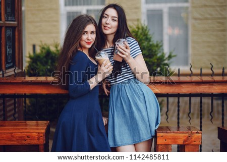 Two beautiful girls in the summer sunny city drink coffee
