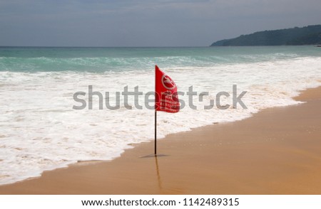 No Swimming Here red flag on a beach in Phuket, Thailand. The warning inscription is in the English, Thai and Russian languages
