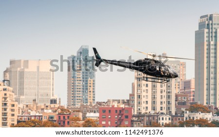 Black helicopter hovering over New York buildings.