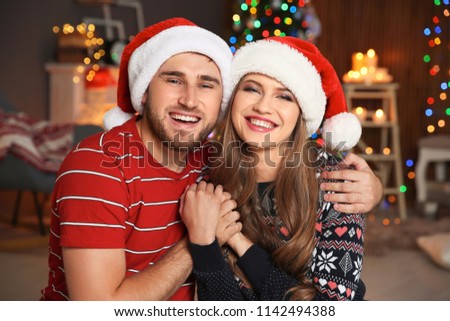 Happy young couple in Santa hats celebrating Christmas at home