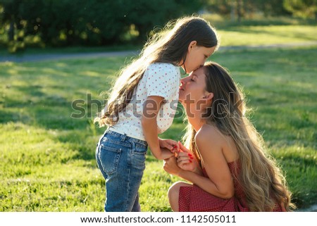 dear daughter long hair kissing her mother in a cocktail dress on the forehead in the park