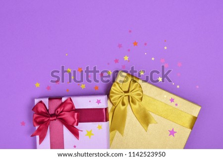 Colored shiny classic gift boxes with satin bows and confetti in the shape of stars as attributes of party on purple background