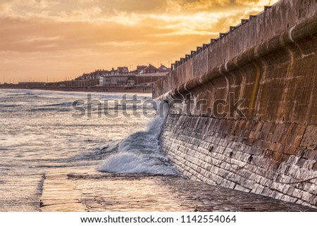 Bridlington, East Yorkshire, on a winter afternoon. A wave splashes against the sea wall. Royalty-Free Stock Photo #1142554064