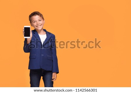 Little boy with smartphone at orange studio background, copy space. Happy child in formal suit playing adult businessman.