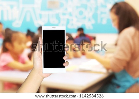Man use mobile phone, blur image of children classroom as background.