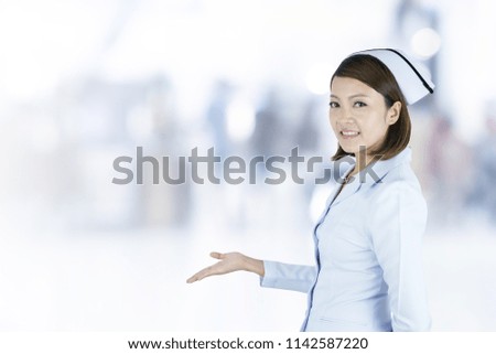 Asian smiling nurse presenting, showing her hand to blank space in hospital blurred background.
