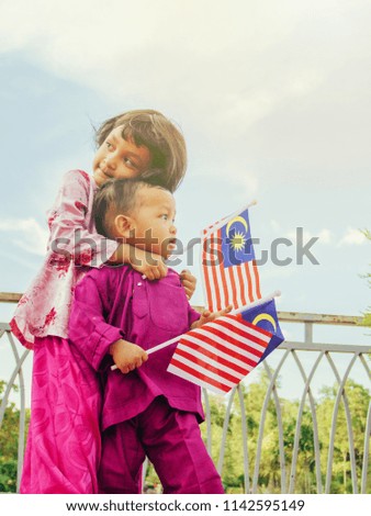 Patriotic siblings holding Malaysian flag hug each other in spirit of Merdeka (Independence Day)