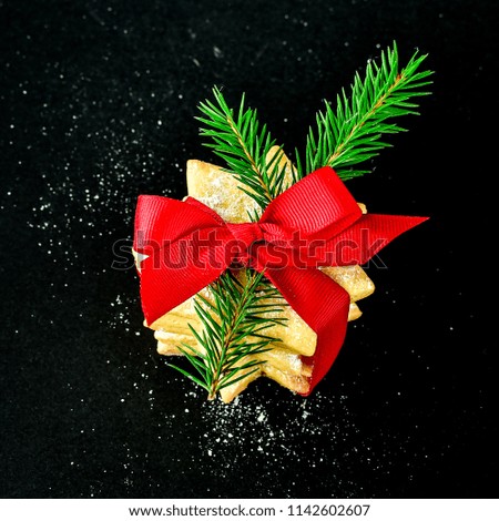 Christmas cookies in the shape of stars decorated with a red ribbon with a bow and a small twig of a Christmas tree on a black table.  selective focus and copy space, card for the new year 2019
