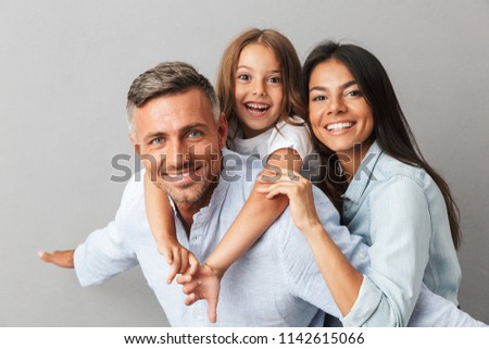 Portrait of a happy family father, mother, little daughter having fun together, father holding little daughter on his back isolated over gray background