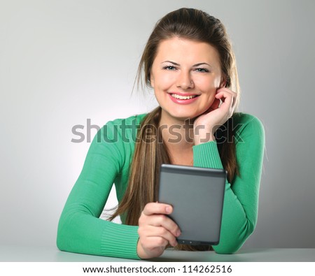 Young woman sitting on the desk and holding computer plane-table , isolated on grey background