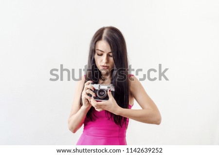 Portrait of a beautiful girl, black hair, red dress, holding in her hands an old vintage photo camera. Looks down.