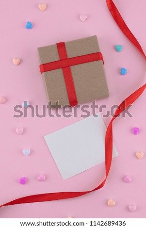 Brown gift box, blank tiny card and red ribbon decorate with pastel heart pattern on pink background