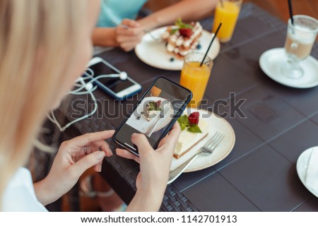 women's hands making photo of sweet dessert on mobile phone while sitting in comfortable restaurant