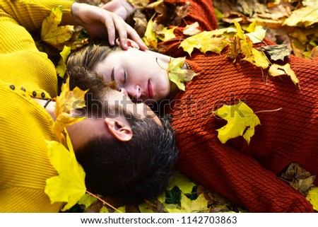 Girl and bearded guy or happy lovers on a date cuddle. Young family and autumn concept. Couple in love lies on dry fallen leaves in park. Man and woman with tender faces on autumn leaves background