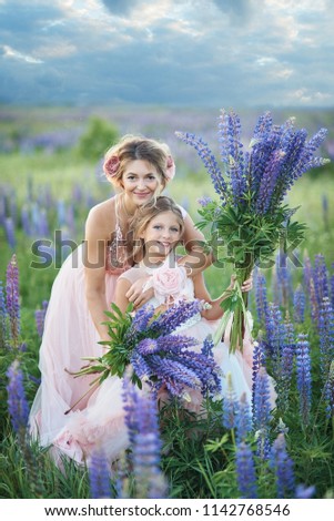 Mother and daughter gathering lupine flowers in beautiful field on sunset. Beautiful girl in violet dress holding a lupine at sunset on the field. The concept of nature and romance