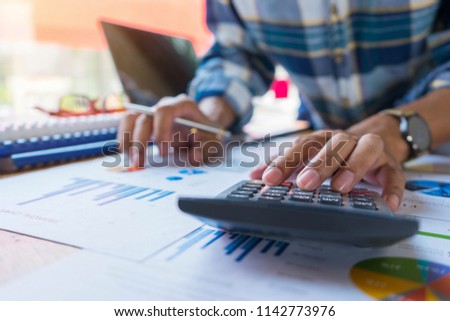 Businessman or accountant working on calculator to calculate financial data report, accounting document and laptop computer. Business financial and accounting concept Royalty-Free Stock Photo #1142773976