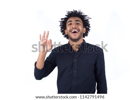 Handsome young man wearing a casual outfit, doing a well-done sign with his left hand and laughing, isolated on white background.