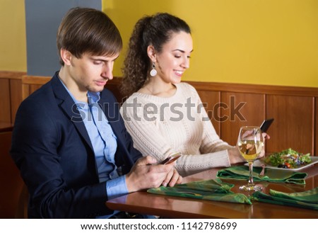 concentrated young man sitting with his girlfriend at restaurant table with smartphones. focus on man