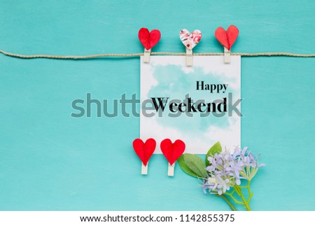 Happy Weekend greeting card with red heart cllip and purple flower on blue wooden background