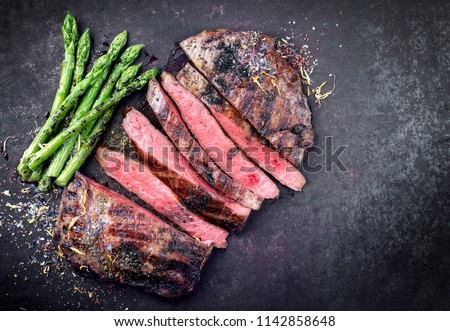 Barbecue dry aged wagyu flank steak sliced with green asparagus as top view on an old rusty board with copy space right Royalty-Free Stock Photo #1142858648