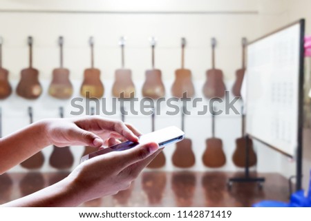 Man use mobile phone, blur image of guitar classroom as background.