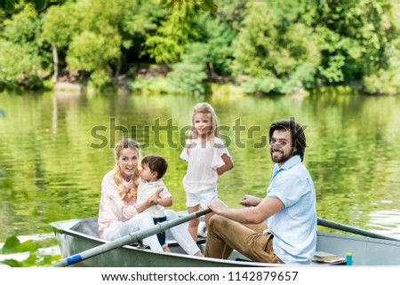 happy young family riding boat on lake at park and looking at camera