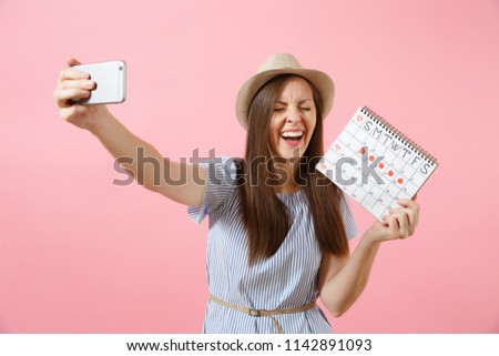 Excited woman in blue dress doing selfie on mobile phone, holding periods calendar for checking menstruation days isolated on pink background. Medical, healthcare, gynecological concept. Copy space
