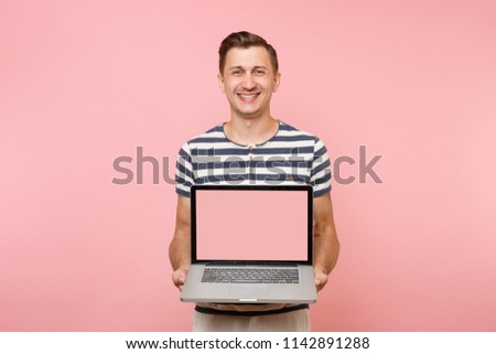 Portrait of young man holding in hand laptop computer with blank black empty screen display copy space isolated on pastel pink background. People sincere emotions lifestyle concept. Advertising area