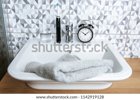 A black electric toothbrush, a clock and a glass of water standing on the bathroom sink