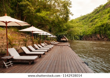 Resort style beach daybeds and white umbrellas by river Kwai, Kanchanaburi, Thailand