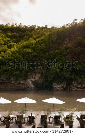 Resort style beach daybeds and white umbrellas by river Kwai, Kanchanaburi, Thailand
