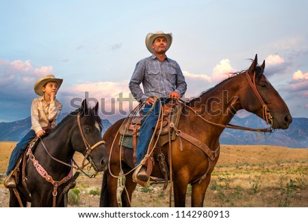 A Cowboy and his son on horseback looking over their ranch lands