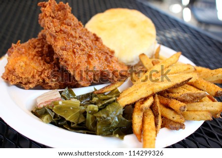 Southern style meal with fried chicken, collard greens with bacon, French fries, and a biscuit.