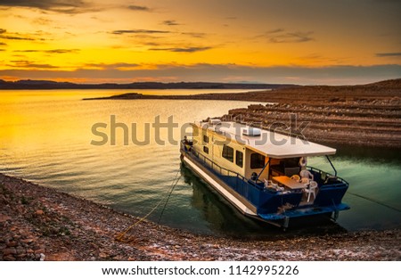 Beautiful and scenic landscape of the Lake Mead National Recreation Area with a houseboat moored to the shores of a bay with a dramatic sky at sunset, Nevada. Vacation and tourism concept. Royalty-Free Stock Photo #1142995226