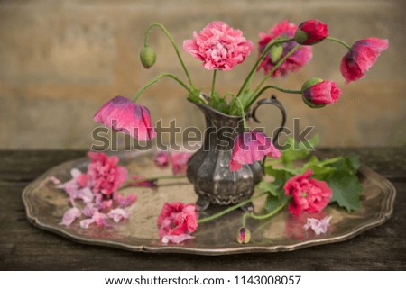A bouquet of pink poppies in an old silver jug, on an old wooden table. Retro style 
