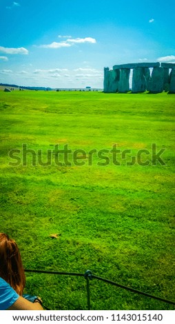 A young, red hair, professional photographer girl is taken pictures of Stonehenge, a prehistoric monument in Wiltshire, England, from multiple angles and perspectives, using zoom and special lens.