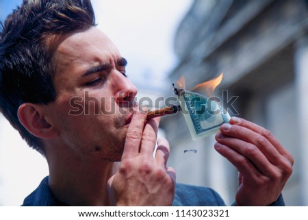 Young brutal businessman lighting cigar with $100 dollar bill 