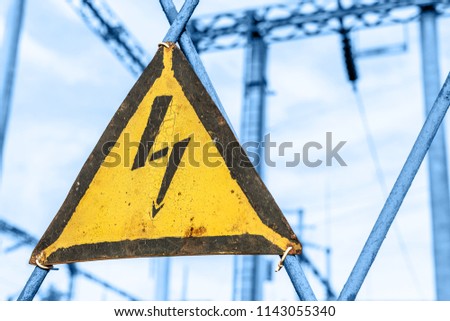 Old aged rusty triangle metal plate with High voltage warning sign. Power station with transformers and electricity distribution lines. Keep out