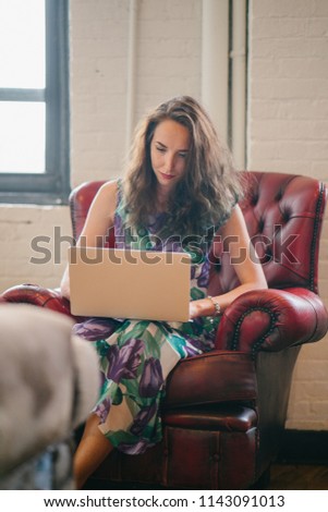 A young and attractive Caucasian woman is a digital nomad and working freelance from a cafe during the day. She is young, attractive, and dynamic and is working on her notebook laptop. 