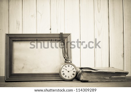 Vintage pocket watch, photo frame, book on a table in front of wooden background