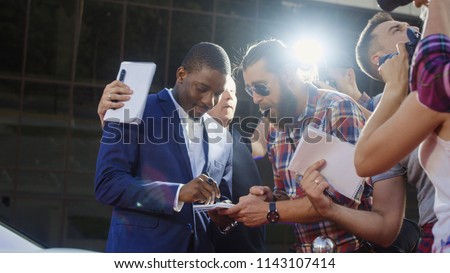 Ethnic celebrity man giving autographs to people on red carpet and makes photos Royalty-Free Stock Photo #1143107414